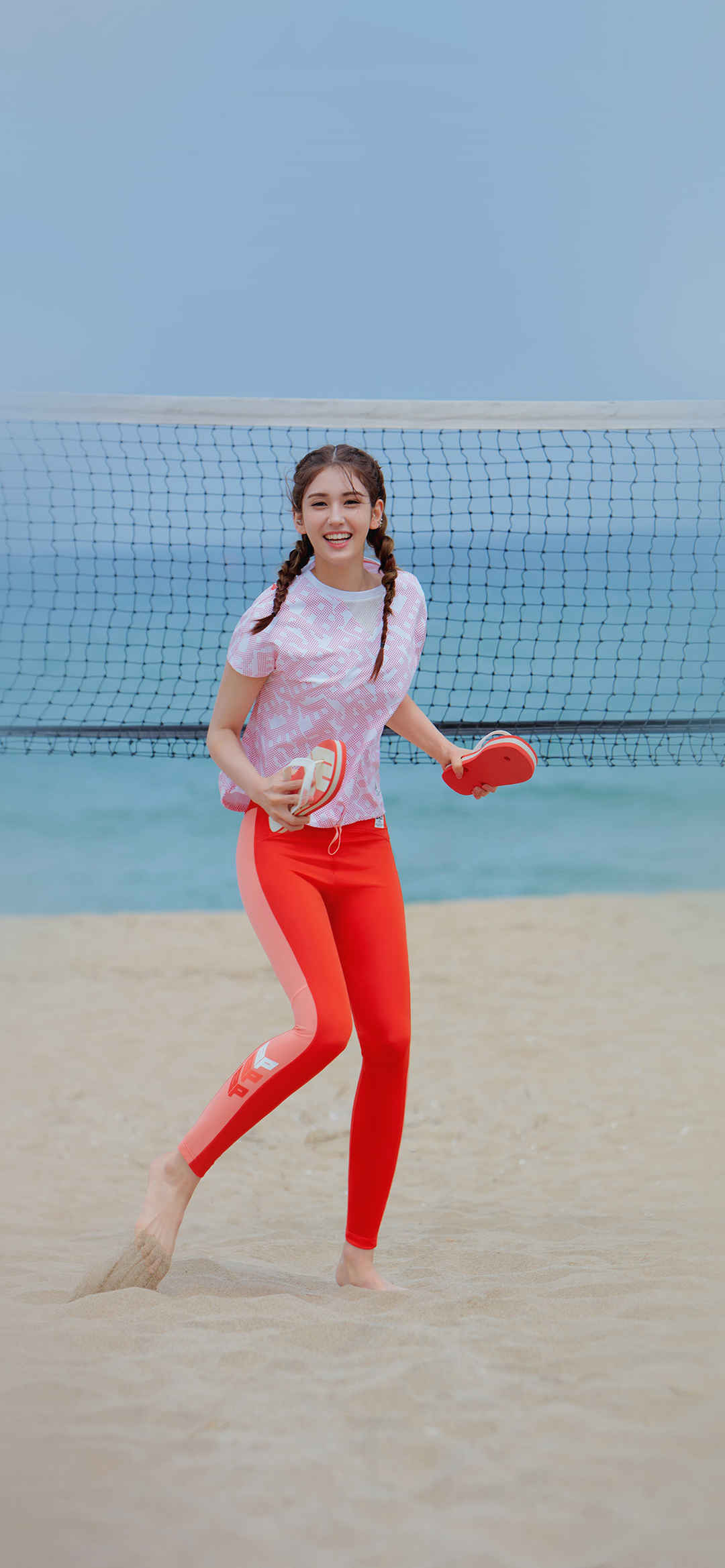 沙滩上穿红色运动裤开心玩沙滩排球的美女高清手机壁纸-
