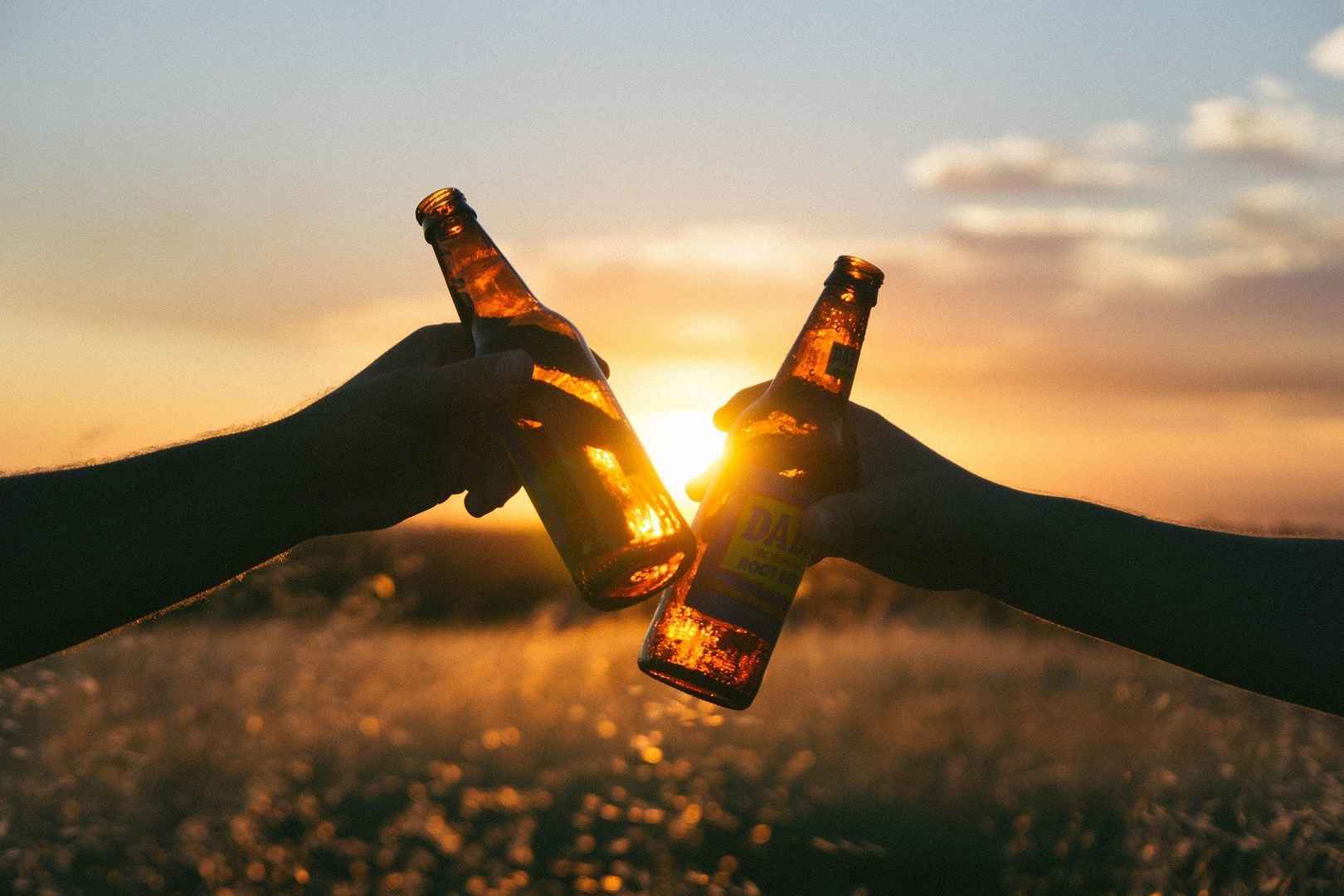 黄昏的阳光下，两只手拿啤酒瓶干杯庆祝的桌面壁纸图片-
