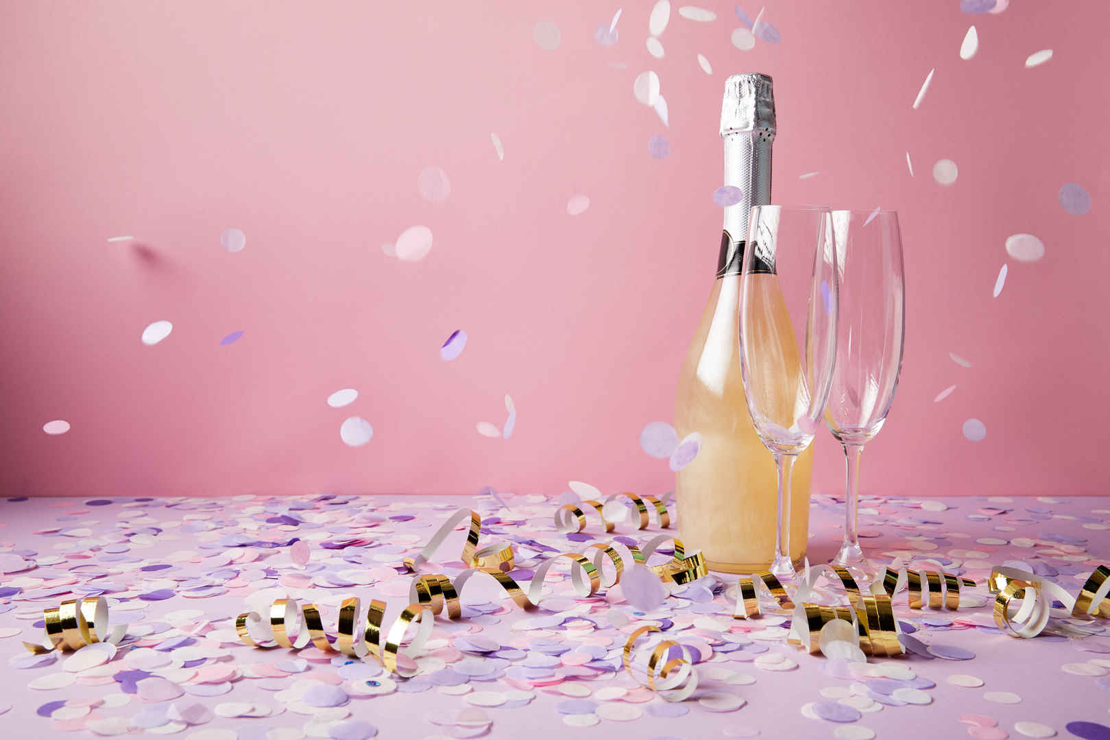 一瓶香槟和玻璃杯在紫罗兰表面上掉落着纸屑片-
