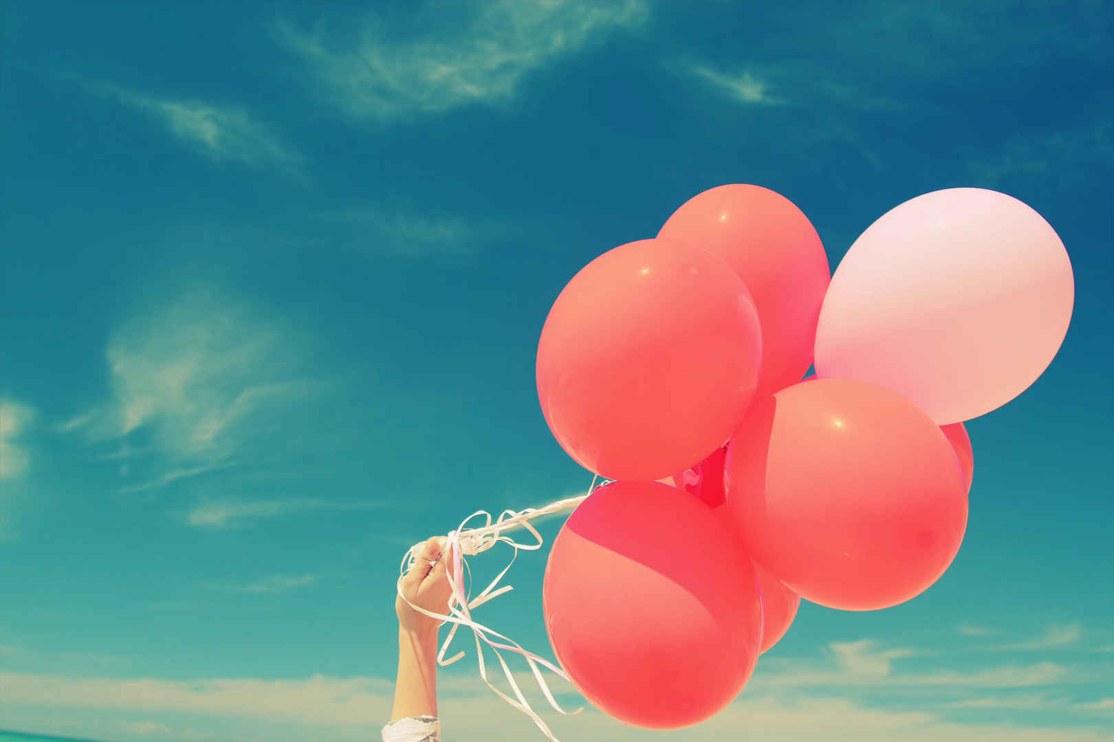 一个女孩手拿红气球举向蔚蓝色的天空-