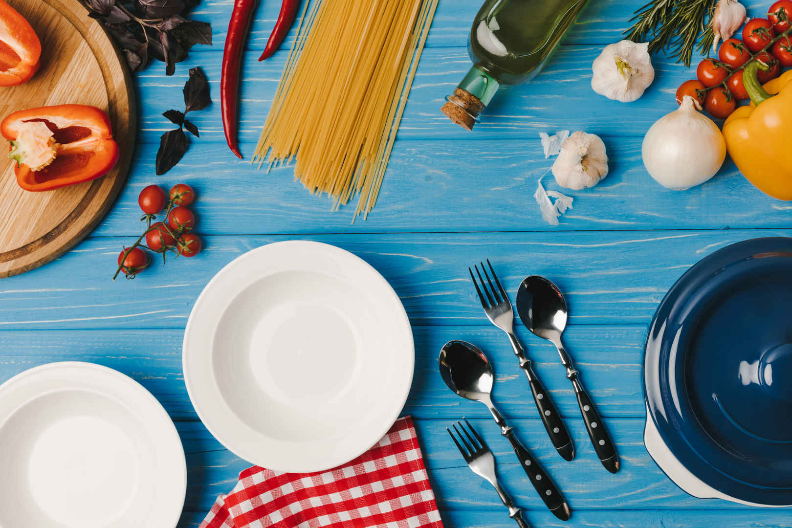 蓝桌上的盘子和未煮过的食物的顶部视图-