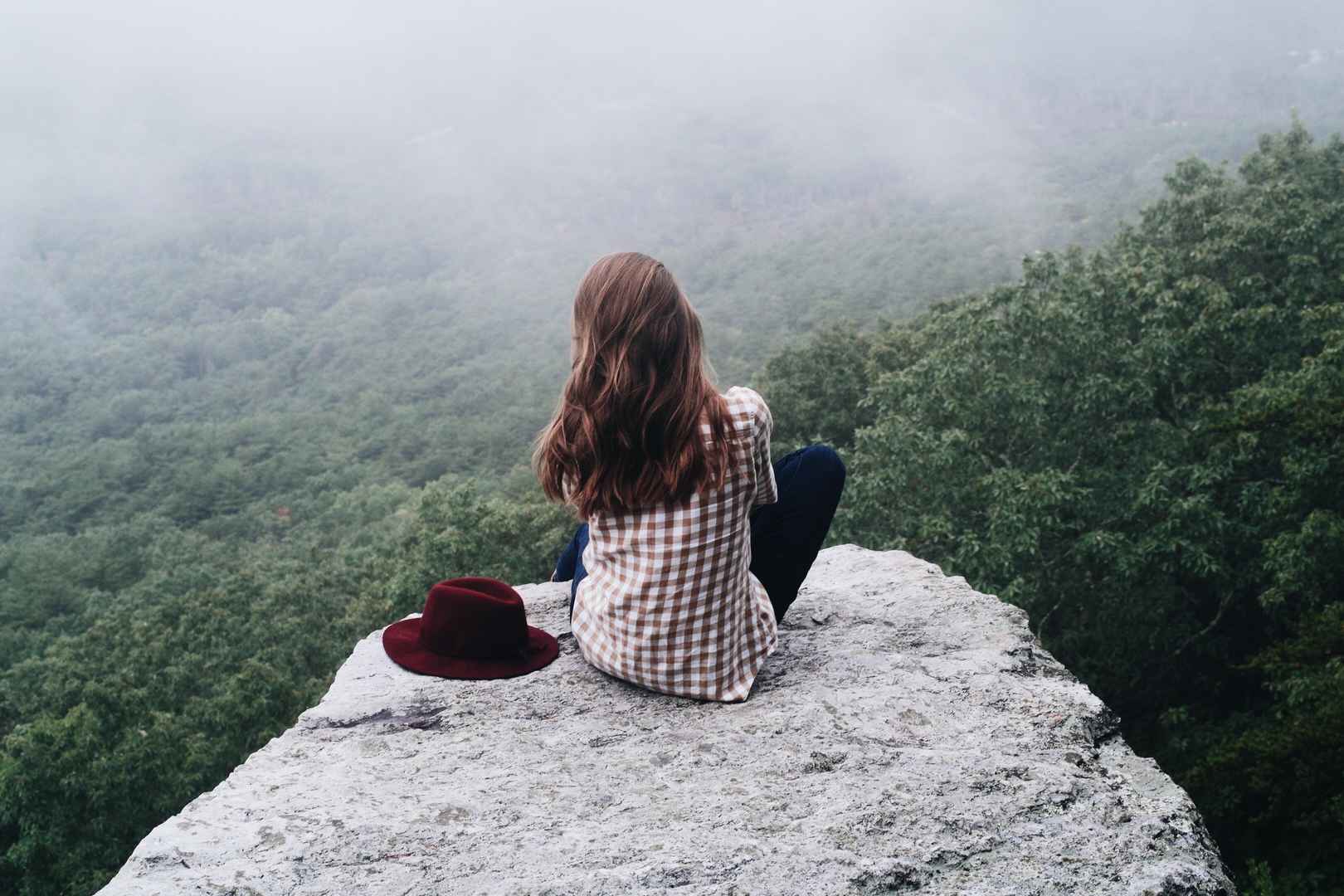 女孩子坐在岩石上眺望深林远方